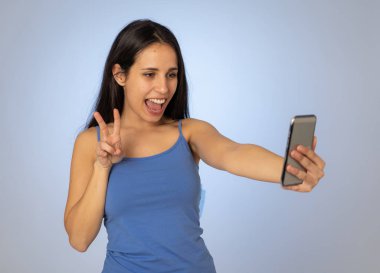 Cep telefonu ile selfie çeken genç serin güzel latin genç kadın Stüdyo çekim eğlenceli ve mobil ve sosyal medya bağımlılığı kullanarak bin yıllık nesil güzel seksi görünümlü.