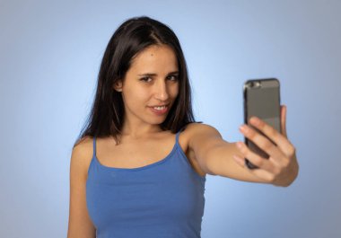 Cep telefonu ile selfie çeken genç serin güzel latin genç kadın Stüdyo çekim eğlenceli ve mobil ve sosyal medya bağımlılığı kullanarak bin yıllık nesil güzel seksi görünümlü.
