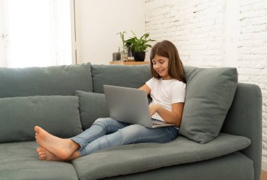 Güzel sevimli sevimli kız öğrenci oynarken ve dizüstü bilgisayar da internette sörf gülümseyerek ve evde kanepede yatarken. Dijital teknoloji, internet kullanımı ve yaşam tarzı konsepti.