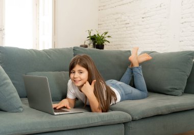 Güzel sevimli sevimli kız öğrenci oynarken ve dizüstü bilgisayar da internette sörf gülümseyerek ve evde kanepede yatarken. Dijital teknoloji, internet kullanımı ve yaşam tarzı konsepti.