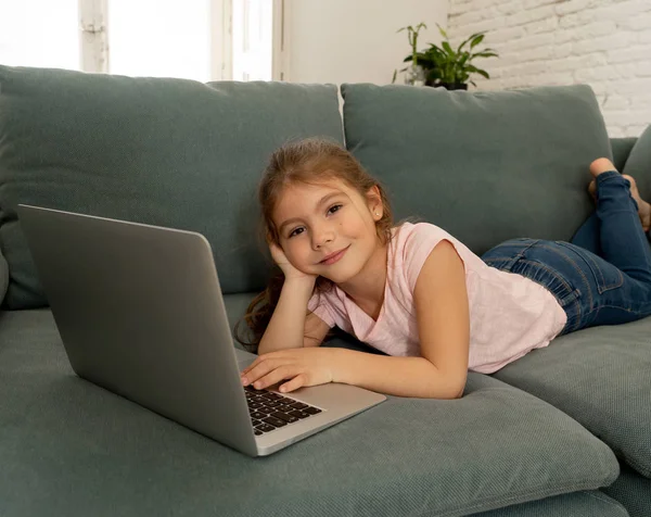 Oldukça sevimli sevimli küçük kız dizüstü bilgisayar kullanarak ve internette gülümseyerek sörf ve evde kanepede yatan eğlenmek. Dijital teknoloji, internet kullanımı ve yaşam tarzı konsepti.