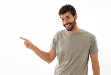 İyi görünümlü genç adam kopya alanı işaret eden neşeli mutlu ve heyecanlı görünümlü. Sakallı hipster metin reklam içeriği için boş arka plan üzerinde izole ilginç bir şey gösteren.