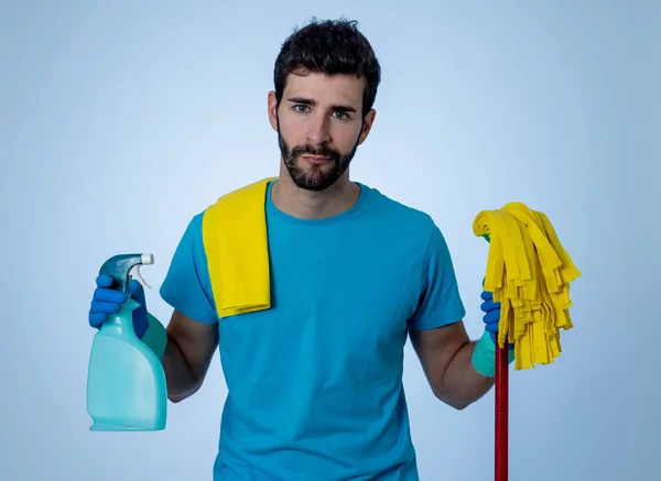 Young attractive man tired and upset holding bucket mop and cleaning spray feeling sad frustrated and lazy in domestic duties concept and men and women gender roles. Isolated on blue background