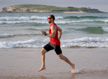 Gün batımında sahilde yalınayak koşan atlet koşucu. Spor adam fitness modeli açık fitness eğitimi, spor, motivasyon ve aktif sağlıklı yaşam tarzı kavramı deniz kıyısında çalışma.