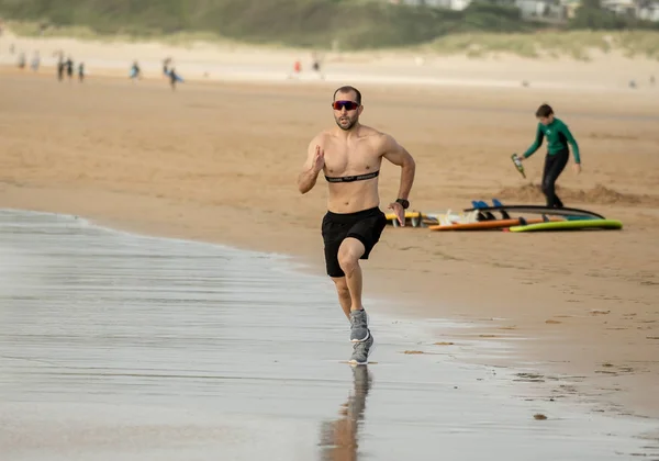 Athlete runner running with heart rate monitor and smart watch on beach. Shirtless fitness man exercising in outdoor training. Advertising style in sports technology healthcare wellness innovation.