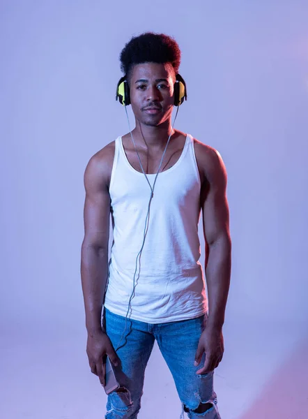 Artistic portrait of strong african american young dancer or DJ with headphones ready to play or dance in disco dance floor neon light in Internet Music festival and online music technology concept.