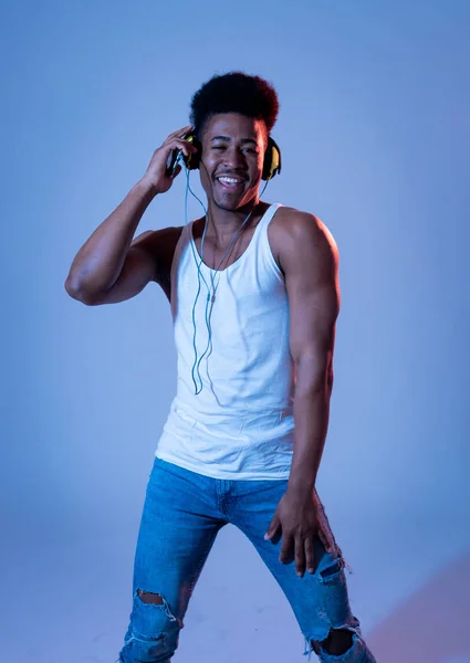 Strong african american young dancer man listening to music online dancing and singing with headphones. Artistic portrait with disco dance floor neon light in Internet Music and technology concept.