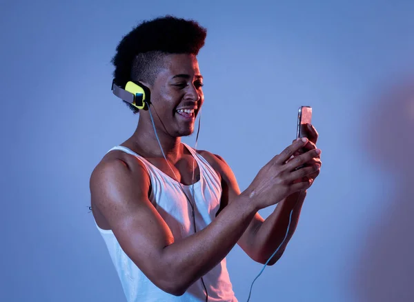 Strong african american young man listening to music in smartphone app looking for best song online with headphones singing and dancing. Portrait with disco dance floor light in Music and technology.
