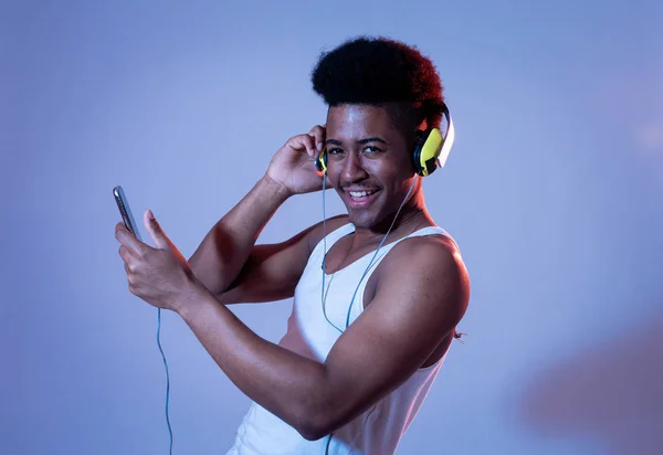 Strong african american young man listening to music in smartphone app looking for best song online with headphones singing and dancing. Portrait with disco dance floor light in Music and technology.