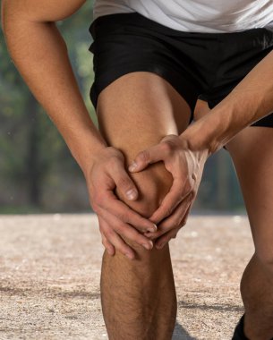 Genç fit adam ağrı içinde elleri ile diz tutarak kas yaralanması kırık diz ağrısı veya kramp açık havada çalışan sırasında acı sonra. Vücut ağrısı ve spor eğitimi yaralanma ve vücut sağlığı.