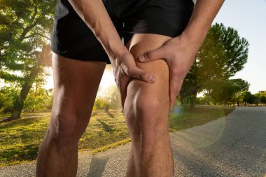 Genç fit adam ağrı içinde elleri ile diz tutarak kas yaralanması kırık diz ağrısı veya kramp açık havada çalışan sırasında acı sonra. Vücut ağrısı ve spor eğitimi yaralanma ve vücut sağlığı.