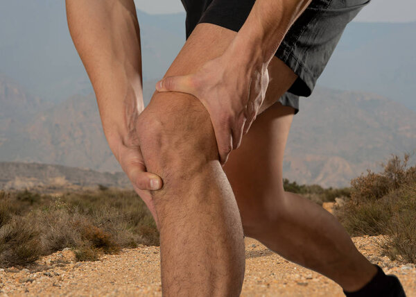 Молодой человек, держащий колено с болью в руках после травмы мышц, сломанного растяжения колена или судороги во время бега на свежем воздухе. В боли в теле и спортивной подготовки травмы и здравоохранения тела
.