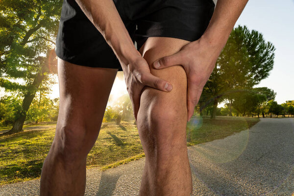 Young fit man holding knee with hands in pain after suffering muscle injury broken knee pain sprain or cramp during outdoors running. In Body pain and sport training injury and body health care.