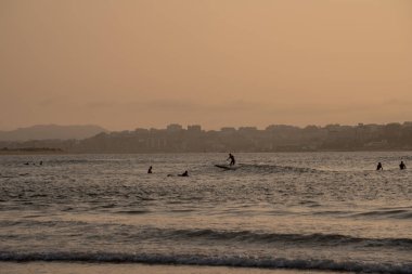 Sörfçü siluetleri geniş görüntü sörf ve güzel güneş ışığı ile gün batımında dalgalar sürme. Reklam tarzı, pazarlama için kopya alanı ile güzel manzara arka plan görüntü.