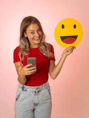 Sosyal medyada yüz ifadelerinde, sosyal ağda, bildirim simgelerinde ve teknoloji iletişiminde sevilmekten heyecan duyan mutlu yüz simgesi tutan çekici genç kadın..