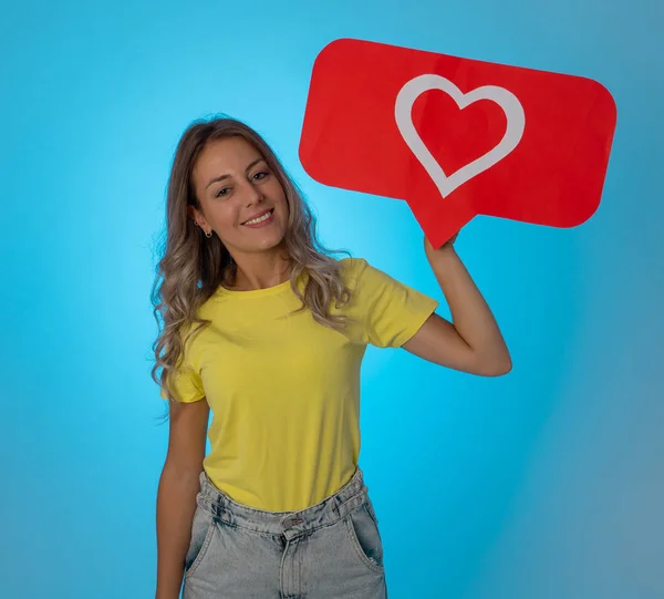Attractive woman holding heart symbol of like and love social media notification icon happy with followers and fans on the internet. Girl loving having likes In social media obsession and networking.