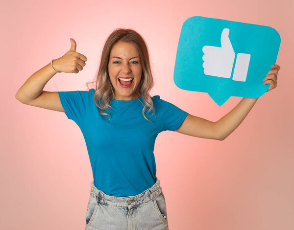 Beautiful young woman holding Like symbol social media notification icon asking followers to like her online comments, blog or business. In Internet obsession, networking and technology connections.