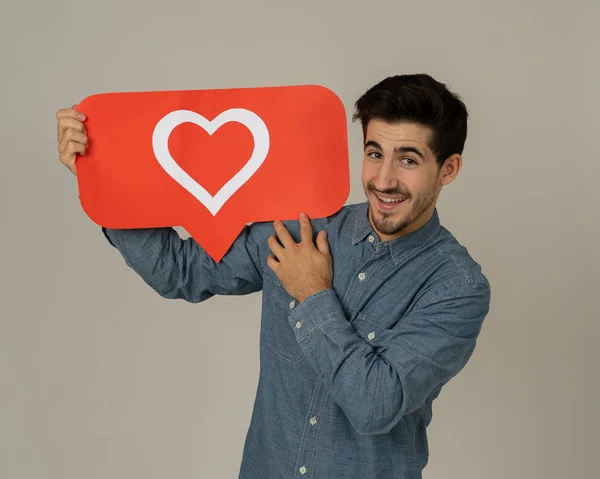 Attractive man holding heart symbol of like and love social media notification icon happy with online followers and fans. Young male loving having likes In social media obsession and networking.
