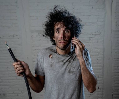 Ev kazasından sonra elektrik kablosu tutan genç bir adamın portresi. Yüzünde yanmış komik bir ifade var. Cep telefonundan yardım istiyor. Elektrik tamiratı ve Diy konsepti.
