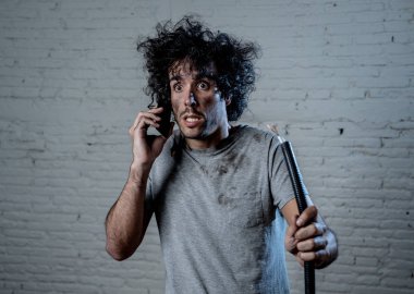 Ev kazasından sonra elektrik kablosu tutan genç bir adamın portresi. Yüzünde yanmış komik bir ifade var. Cep telefonundan yardım istiyor. Elektrik tamiratı ve Diy konsepti.