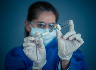 COVID-19 Coronavirus aşısı. Sars-CoV-2 virüsünü inceleyen şırıngalı bir bilim adamı aşı araştırması için klinik deneylere hazır. Kadın araştırmacı laboratuarda potansiyel aşıyı test ediyor..