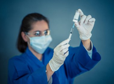 COVID-19 Coronavirus aşısı. Sars-CoV-2 virüsünü inceleyen şırıngalı bir bilim adamı aşı araştırması için klinik deneylere hazır. Kadın araştırmacı laboratuarda potansiyel aşıyı test ediyor..