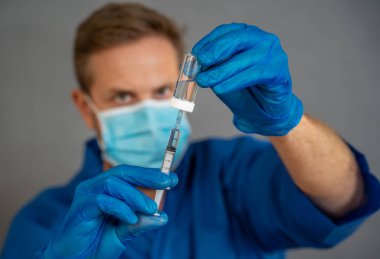 COVID-19 Coronavirus aşısı. Sars-CoV-2 virüsünü inceleyen şırıngalı bir bilim adamı aşı araştırması için klinik deneylere hazır. Erkek araştırmacı laboratuvarda potansiyel aşıyı test ediyor..
