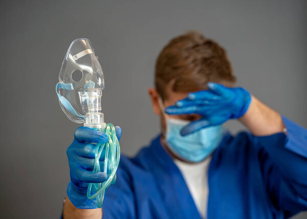 COVID-19 Outbreak. Exhausted Doctor holding non- invasive ventilator. Medical treatment and lack of equipment for coronavirus infected patients with SARS. Shortage of medical ventilators in hospitals.