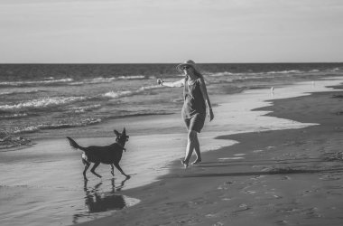Güzel, olgun, emekli bir kadın ve evcil bir köpek boş kumsalda birlikte yürüyor. Açık havada umut ve Coronavirus kilitleme kavramından sonra yeni normal hayata dönüş egzersizleri..