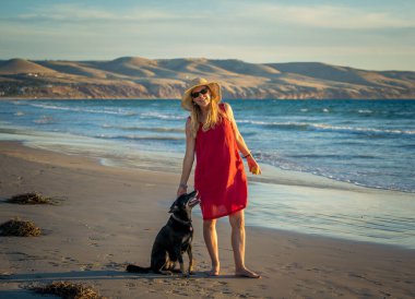 Güzel, olgun, emekli bir kadın ve evcil bir köpek boş kumsalda birlikte yürüyor. Açık havada umut ve Coronavirus kilitleme kavramından sonra yeni normal hayata dönüş egzersizleri..