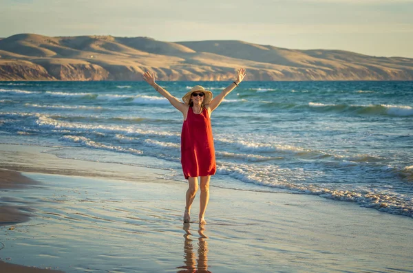 快乐迷人的成熟女人穿着红色的衣服 在户外享受着自由的海滩 张开双臂满怀希望地在放宽了验尸检疫之后 回到生活 户外和新的正常概念 — 图库照片