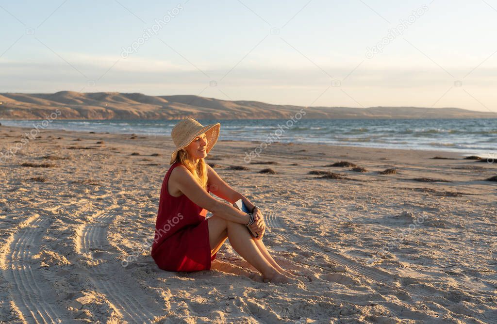 Happy attractive Mature woman in red dress enjoying outdoors and freedom on the beach, open arms outstretched in hope after coronavirus quarantine eased. Back to life, outdoors and new normal concept.