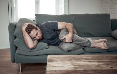 Mutsuz, bunalımlı, beyaz erkek, oturma odasındaki kanepede ağlıyor. Evde kendini yalnız ve çaresiz hissediyor. İş stresi, işsizlik, endişe, kalp kırıklığı ve depresyon konsepti