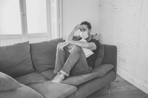 自宅のリビングルームのソファで保護顔マスクを持つ悲しい男は 疲れやコロナウイルスのロックダウンや社会的距離の中での苦しみうつ病を心配感じています 精神衛生と隔離の概念 — ストック写真