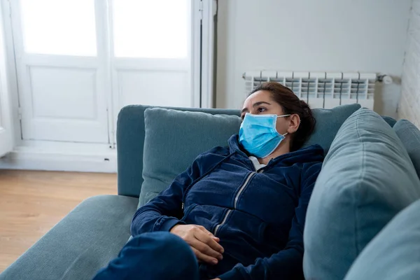 Sorgsen Latinamerikansk Kvinna Med Skyddande Ansiktsmask Hemma Soffa Känsla Trött — Stockfoto