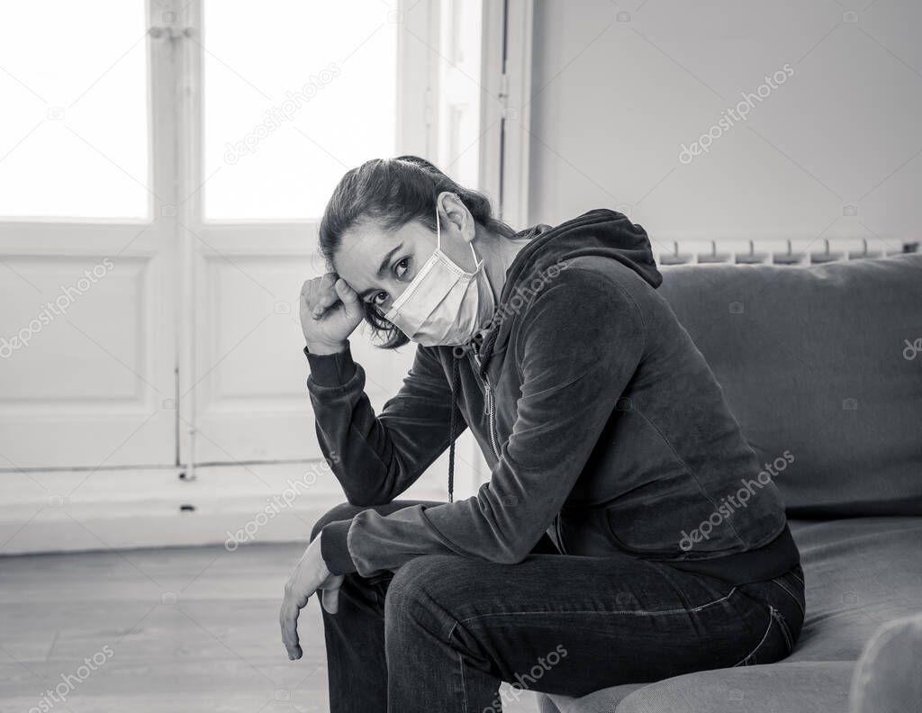 Sad latin woman with protective face mask at home living room couch feeling tired and worried suffering depression amid coronavirus lockdown and social distancing. Mental Health and isolation concept.