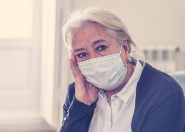 Yalnız, koruyucu maskeli yaşlı dul bir kadın evde yalnız başına ağlıyor, üzgün ve endişeli bir koca ve aile COVID-19 'da kayıp, tecrit, sosyal mesafeler ve akıl sağlığı.