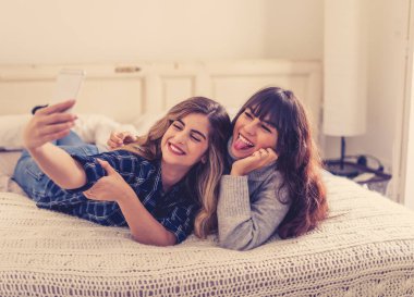 COVID-19, evde kal. Bağlantıda kal. Mutlu kadın kız arkadaşlar Coronavirus kilitleme ve sosyal mesafeler sırasında cep telefonu kullanarak arkadaşlarıyla görüntülü konuşma ya da çevrimiçi grup ev partileri yapıyorlar..