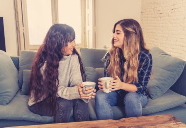 COVID-19 tecrit. Kendinden emin ve iyimser kadın sevgililer birlikte konuşuyor ve sıcak bir şeyler içiyor izole halde evde birlikte kalıyorlar. Evde kalın Sağlığınıza ve güvenliğinize dikkat edin.
