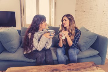 COVID-19 tecrit. Kendinden emin ve iyimser kadın sevgililer birlikte konuşuyor ve sıcak bir şeyler içiyor izole halde evde birlikte kalıyorlar. Evde kalın Sağlığınıza ve güvenliğinize dikkat edin.