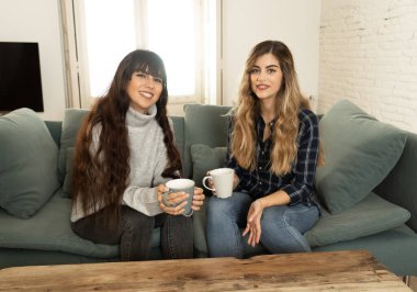 COVID-19 tecrit. Kendinden emin ve iyimser kadın sevgililer birlikte konuşuyor ve sıcak bir şeyler içiyor izole halde evde birlikte kalıyorlar. Evde kalın Sağlığınıza ve güvenliğinize dikkat edin.