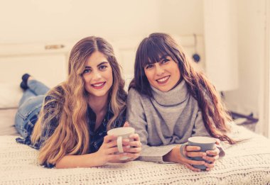 COVID-19 tecrit. Kendinden emin ve iyimser kadınlar en iyi kız arkadaşlar yatakta konuşurken ve gülerken sıcak içecekler evde yalnızken. Evde kal. Sağlığını ve güvenliğini koru..