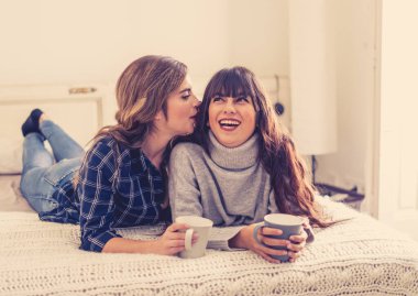 COVID-19 tecrit. Kendinden emin ve iyimser kadınlar en iyi kız arkadaşlar yatakta konuşurken ve gülerken sıcak içecekler evde yalnızken. Evde kal. Sağlığını ve güvenliğini koru..