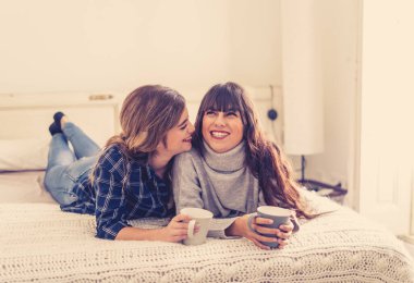 COVID-19 tecrit. Kendinden emin ve iyimser kadınlar en iyi kız arkadaşlar yatakta konuşurken ve gülerken sıcak içecekler evde yalnızken. Evde kal. Sağlığını ve güvenliğini koru..