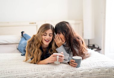COVID-19 tecrit. Kendinden emin ve iyimser kadınlar en iyi kız arkadaşlar yatakta konuşurken ve gülerken sıcak içecekler evde yalnızken. Evde kal. Sağlığını ve güvenliğini koru..