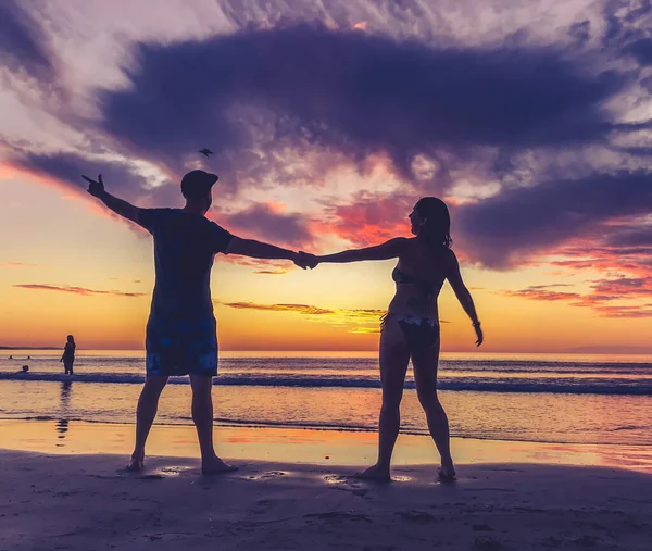 Silhouettes of couple in love feeling free during honeymoon at spectacular beach sunset. Man and woman silhouette celebrating love freedom and health. Romantic escapes holidays and wellness concept.