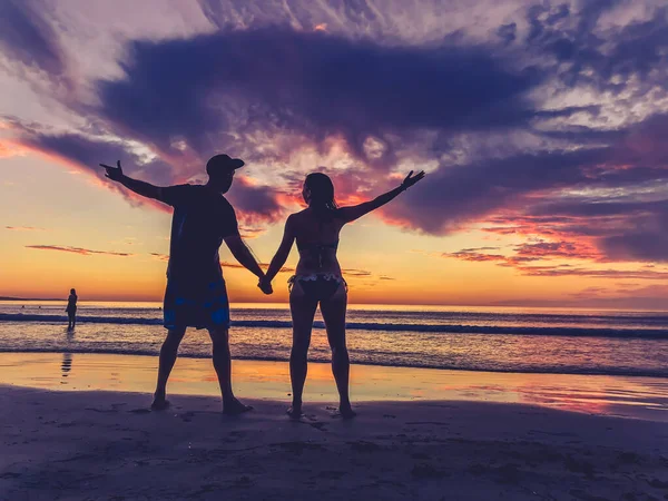 Silhouettes of couple in love feeling free during honeymoon at spectacular beach sunset. Man and woman silhouette celebrating love freedom and health. Romantic escapes holidays and wellness concept.