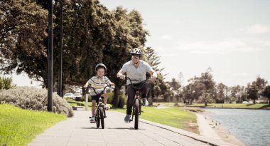 Mutlu baba ve oğul göl kenarında bisiklete biniyorlar. Baba ve oğul parkta bisikletleriyle eğleniyorlardı. Mutlu aile, açık hava aktiviteleri, çocukluk ve ebeveynlik kavramı.