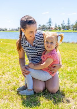 Anne ve kızının göl kenarında eğlenirken pozitif bir portresi. Parkta annesi olan sevimli küçük bir kız. Aşk, aile zamanı, annelik, çocukluk ve açık hava kavramı.