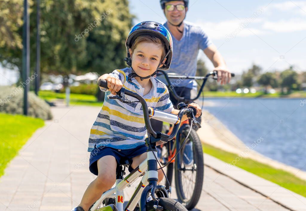 Happy Father and son riding their bicycles by the lake. Father and son having fun together on their bikes in the park. Happy family, outdoors activities, childhood and parenting concept.